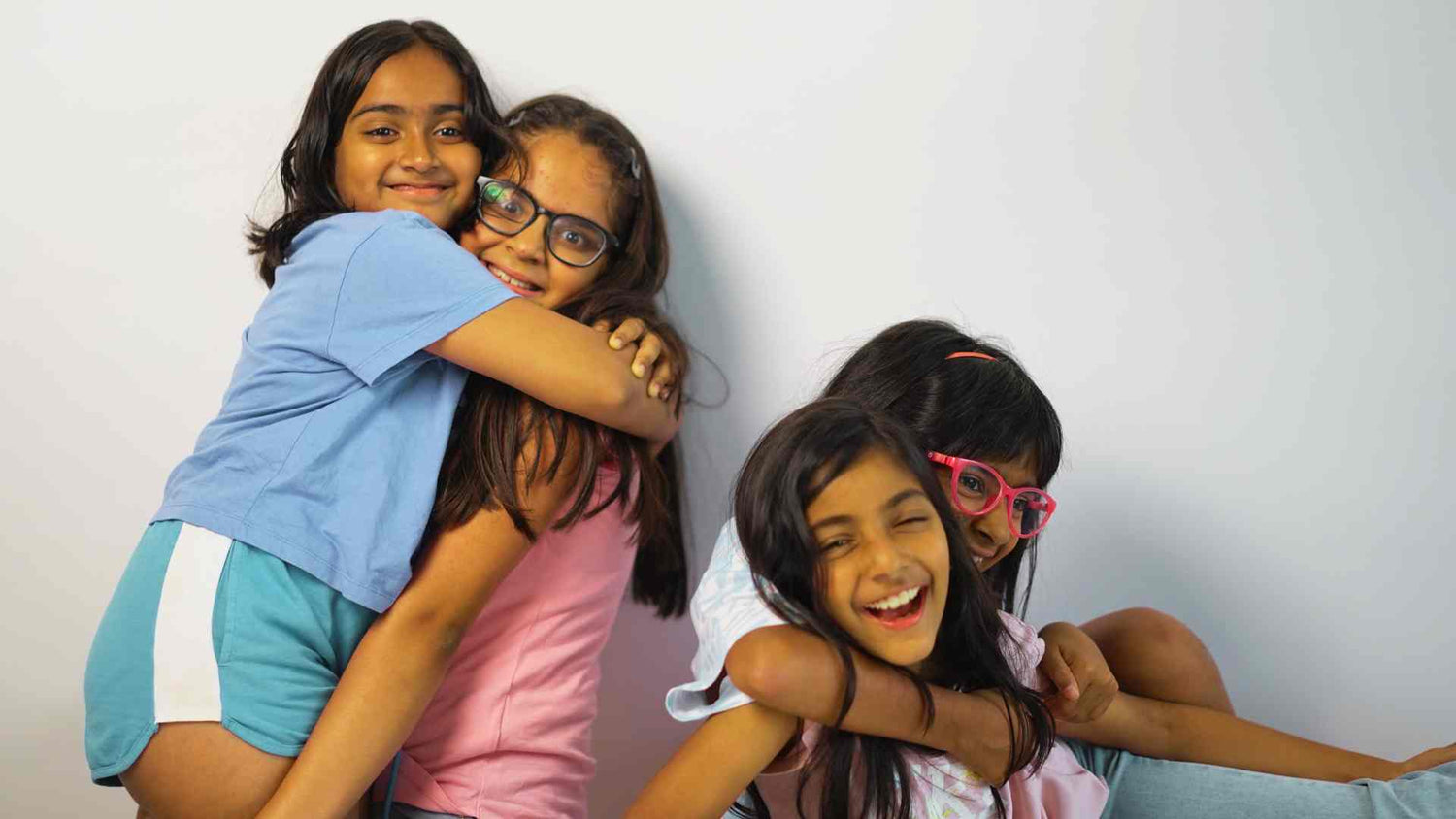 Four young girls hugging each other against a plain background